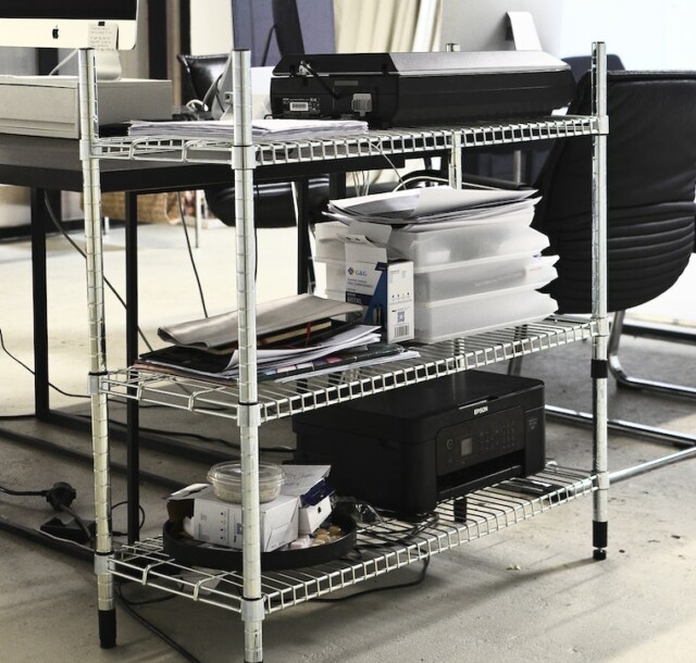 Iron shelves with hardware placed near table with computers in office in daytime
